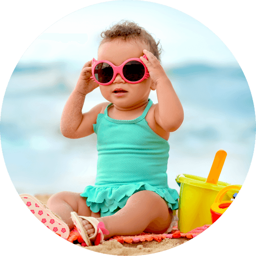 Baby in green swimming costime and sunglasses at the beach